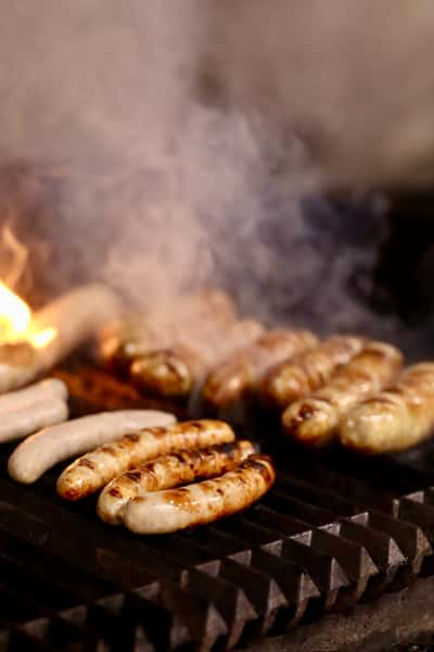 sausages grilling over open flame with smoke rising in kitchen