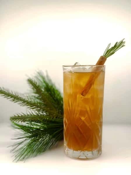amber cocktail with ice and garnish on a bar counter with greenery