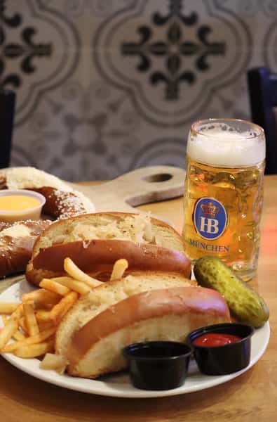 bratwurst sandwich with fries, pickle, and German beer on table