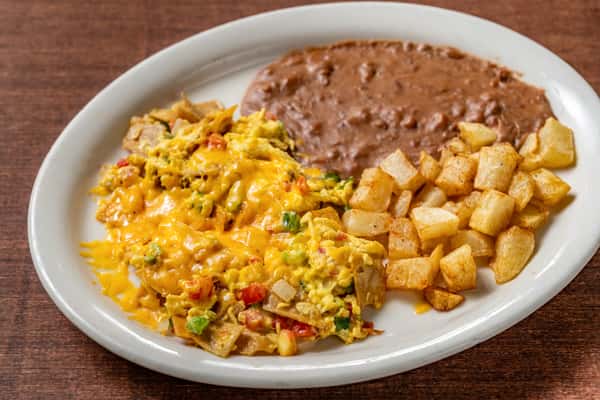 Hearty Mexican breakfast plate with scrambled eggs and tortilla strips (chilaquiles), topped with melted cheddar, served with refried beans and crispy diced potatoes.