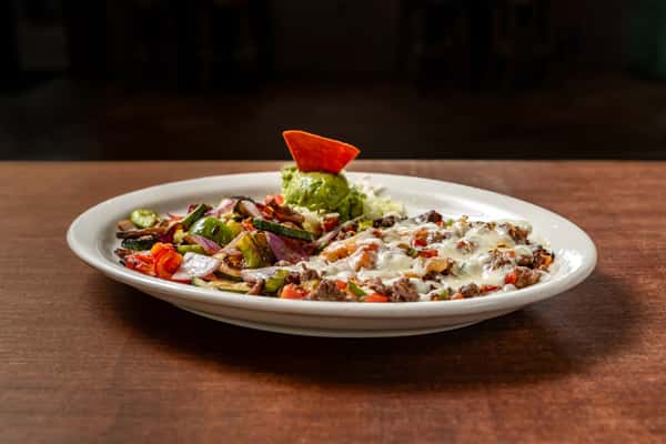 Sizzling grilled beef fajita mix topped with melted cheese and served alongside sautéed bell peppers, onions, and guacamole salad on a white plate.