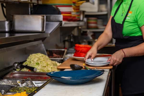 Behind-the-scenes look at a Mexican restaurant kitchen with fresh ingredients, a blue serving plate, and staff preparing dishware.