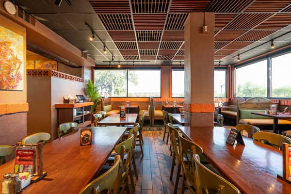 Spacious and warmly lit Mexican restaurant dining area featuring rustic wooden tables, cozy booth seating, and large windows offering natural light and scenic views.