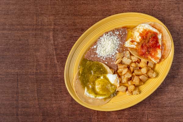 Huevos rancheros breakfast plate with two fried eggs—one topped with salsa and the other with green tomatillo sauce—served with refried beans, diced potatoes, and a crispy tortilla.