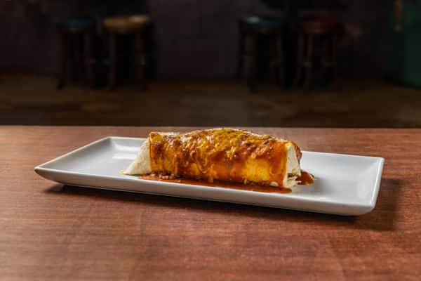 Hearty burrito drenched in red sauce and melted cheese, photographed against a restaurant backdrop on a modern white plate.