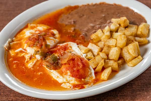 Classic huevos rancheros breakfast with two eggs topped in spicy red salsa, served with crispy breakfast potatoes and refried beans on a white plate—perfect for savory brunch menus.