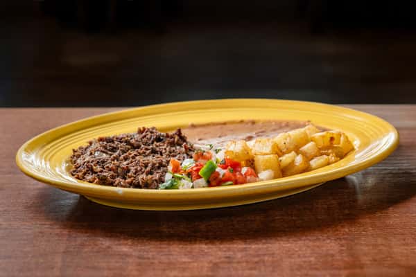Savory shredded beef with refried beans, crispy breakfast potatoes, and fresh pico de gallo, presented on a bright yellow oval plate.