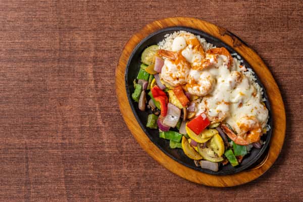 Sizzling shrimp fajitas over rice with grilled bell peppers, onions, and squash, topped with melted cheese, served on a cast iron skillet.