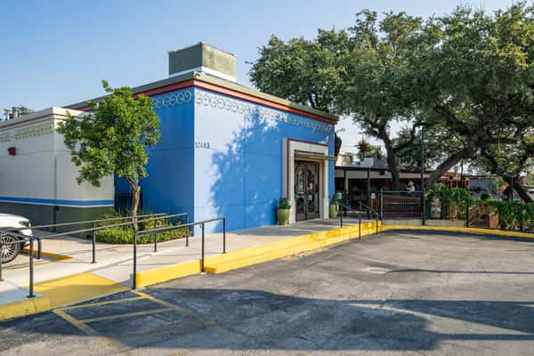 Bright blue-painted building exterior of a Mexican restaurant, with prominent entryway and ramp access, shaded by mature trees—creates a welcoming and accessible curb appeal.