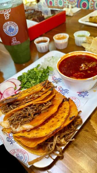 Birria tacos with shredded beef, served with consommé, chopped onion, cilantro, radish slices, and assorted dipping sauces.
