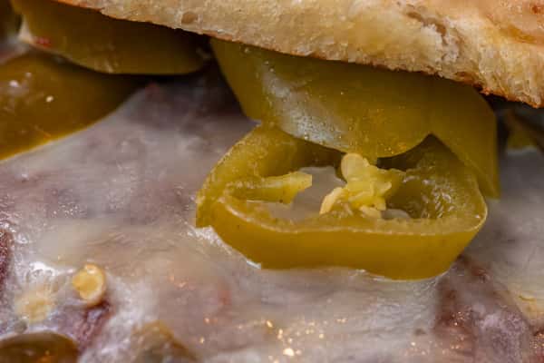 Extreme close-up of sliced jalapeños atop melted cheese and seared meat patty — perfect for spicy burger product features or culinary ingredient highlights.