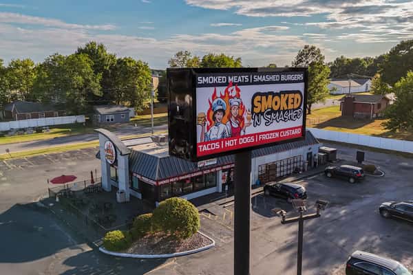 Aerial view of Smoked N' Smashed restaurant with large billboard signage showcasing branding for tacos, hot dogs, and frozen custard — great for business listings and franchise promotions.