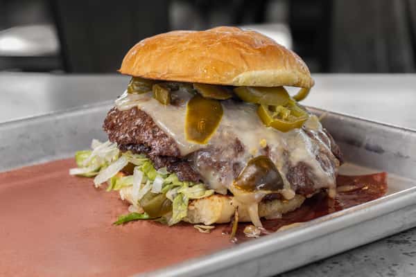 Smashburger topped with melted pepper jack cheese, sliced jalapeños, shredded lettuce, and onions on a toasted bun — bold and spicy American burger option.
