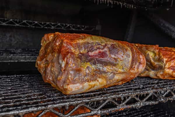 Large seasoned pork shoulder smoking low and slow inside a barbecue pit — capturing authentic BBQ preparation with a flavorful dry rub.