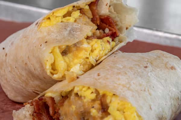 Close-up of a loaded breakfast burrito with fluffy scrambled eggs, crispy bacon, and melted cheese wrapped in a warm tortilla — indulgent and savory breakfast wrap.