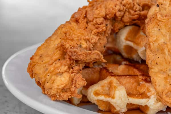 Close-up of crispy fried chicken tenders served on top of golden waffles with syrup drizzle — perfect for Southern comfort food or brunch marketing.