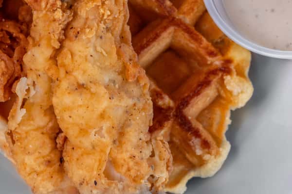 Fried chicken tenders served on Belgian waffles with a side of creamy dipping sauce — perfect for diner or brunch food advertising.