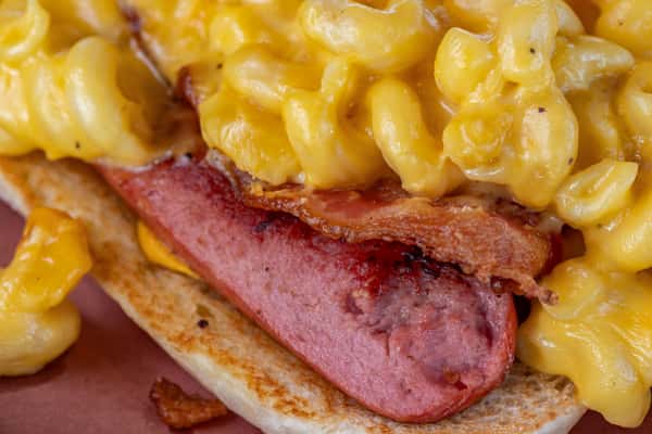 Grilled hot dog topped with crispy bacon and creamy mac and cheese, served on a toasted bun — a bold twist on classic American comfort food.