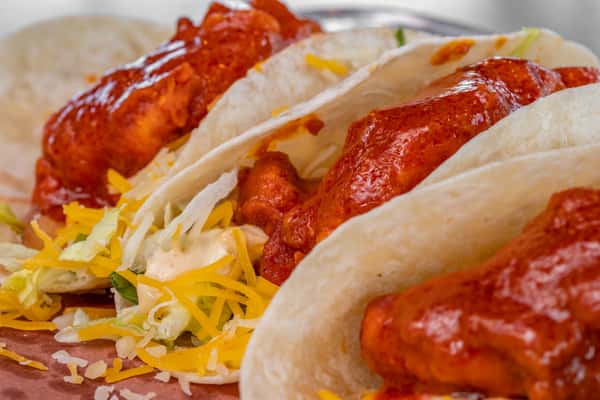 Soft flour tortillas filled with crispy buffalo chicken tenders, shredded lettuce, and a blend of cheddar and Monterey Jack cheeses — spicy and flavorful Tex-Mex-style tacos.
