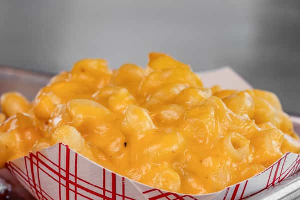 reamy baked mac and cheese served in a red-checkered paper tray, featuring tender elbow pasta coated in rich, melted cheddar — a classic American comfort side dish.