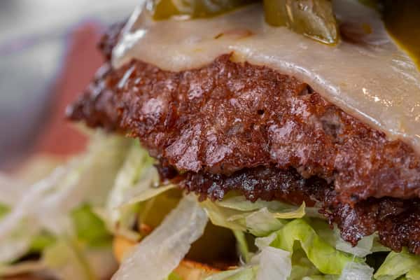 Close-up of a seared smash burger patty topped with melted cheese and jalapeños, served on a bed of shredded lettuce — ideal for gourmet burger advertising.