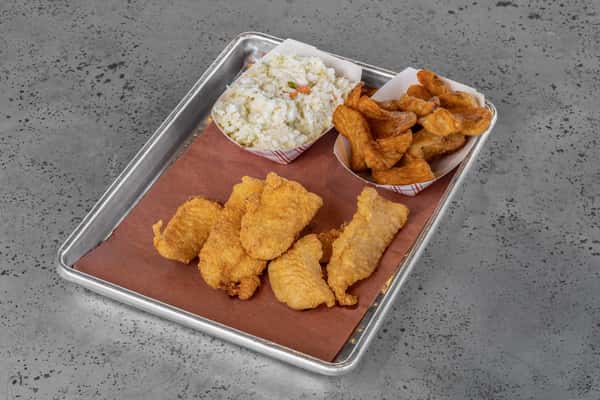 Crispy fried fish fillets served with seasoned potato wedges and creamy coleslaw in paper trays on a metal serving tray — a classic American fish fry mea