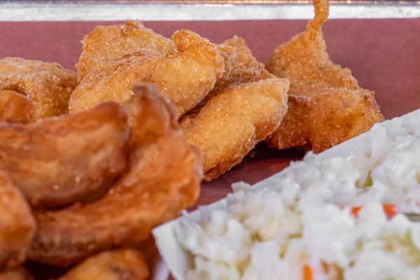 Golden fried chicken bites served on a metal tray with crispy potato wedges and a side of creamy coleslaw — classic Southern-inspired comfort food perfect for casual dining or food truck menus.