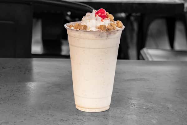 Vanilla milkshake served in a clear plastic cup, topped with whipped cream, crushed peanuts, and a maraschino cherry — classic American diner dessert perfect for summer menus.
