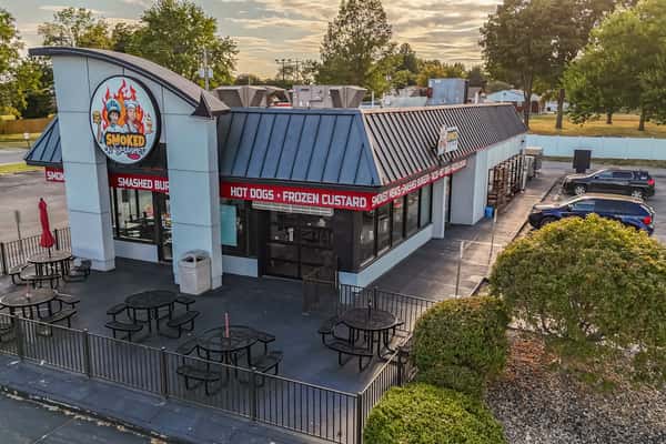 Exterior view of Smoked N Smashed restaurant, showcasing outdoor seating and signage for hot dogs, frozen custard, smashed burgers, and smoked meats — ideal for casual, family-friendly dining.