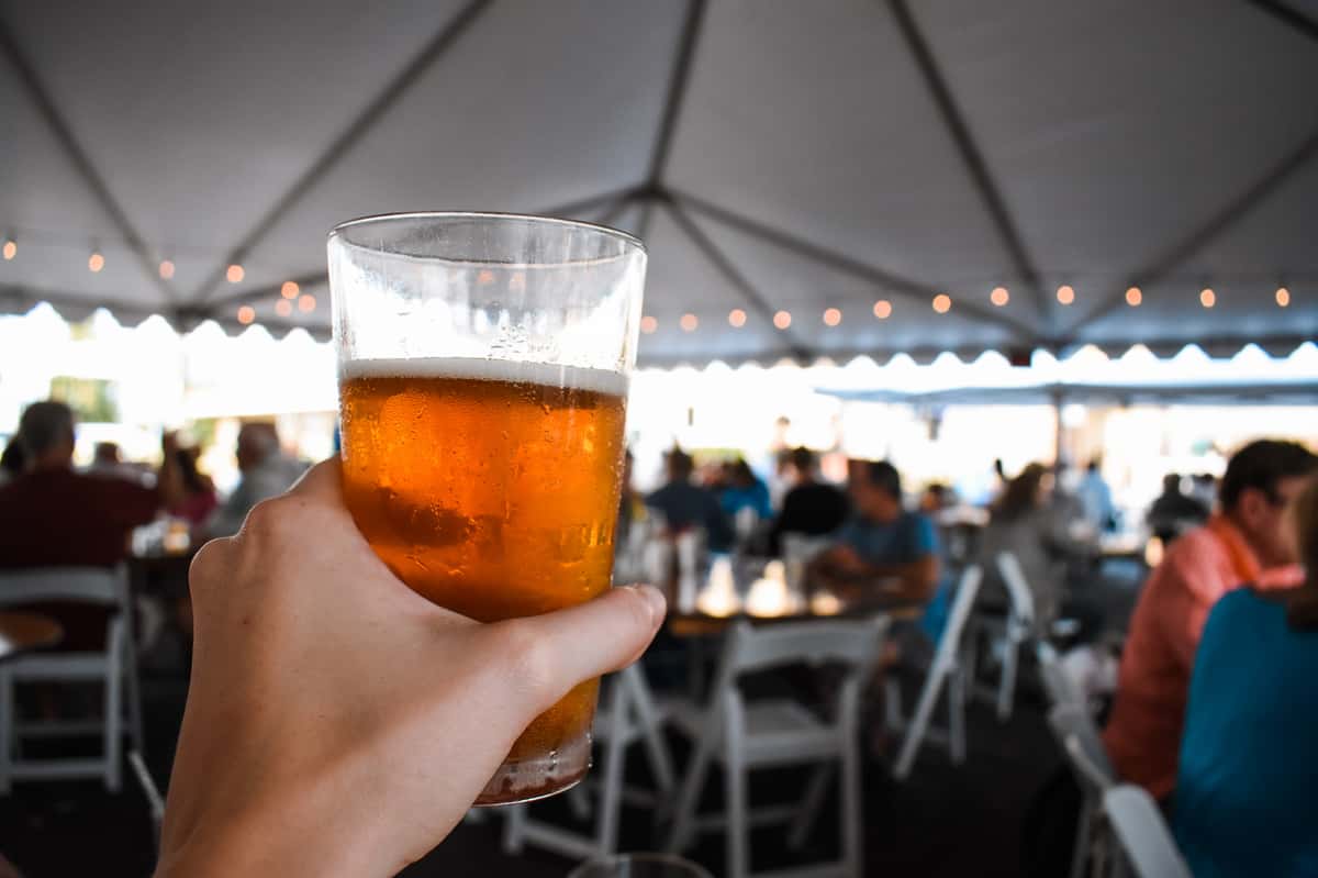 Photo of a hand holding a draft beer with an entertainment tent in the background
