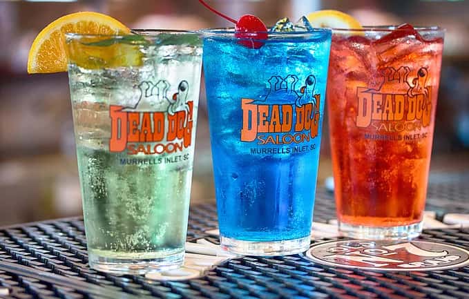 Three different drinks in Dead Dog Saloon labeled glasses