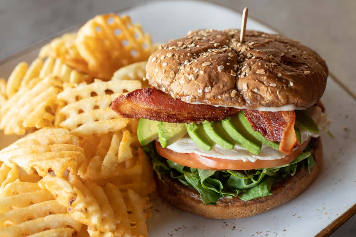 Turkey sandwich with sliced avocado and bacon with a side of waffle fries.