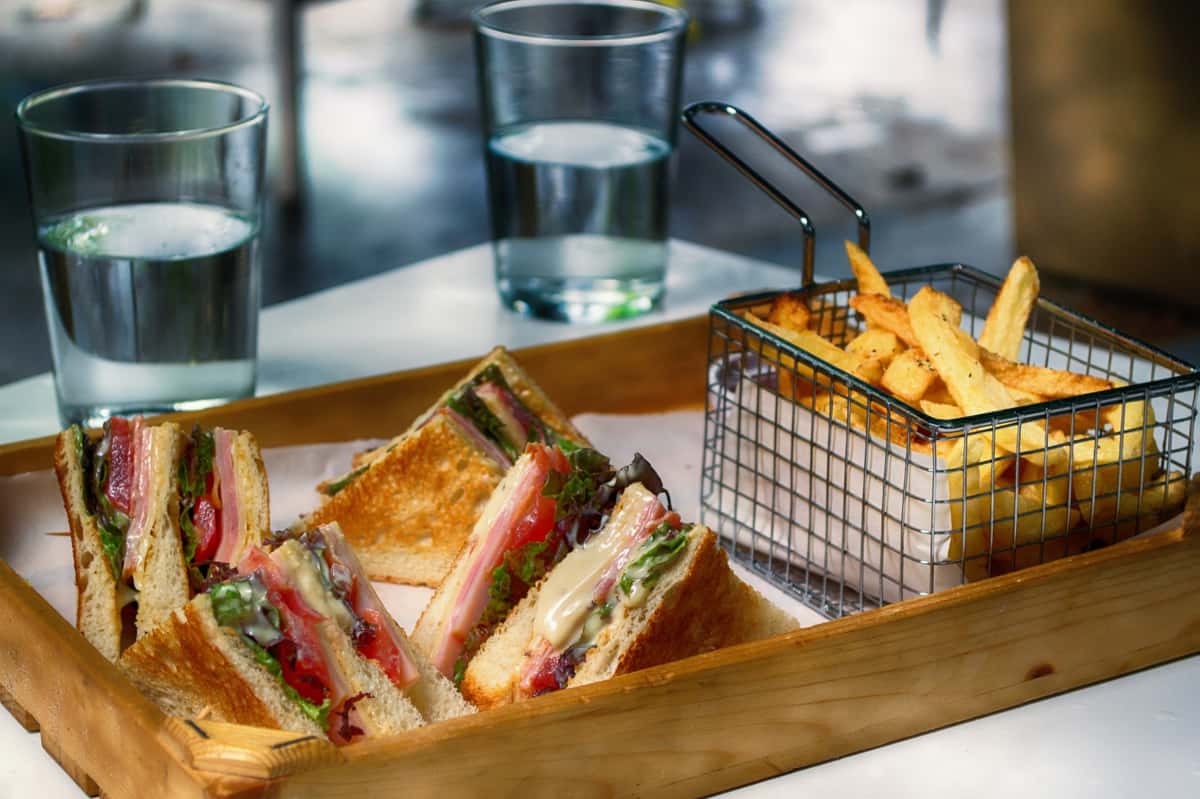 Wooden tray with a variety of sandwiches and a metal serving fry basket of fries