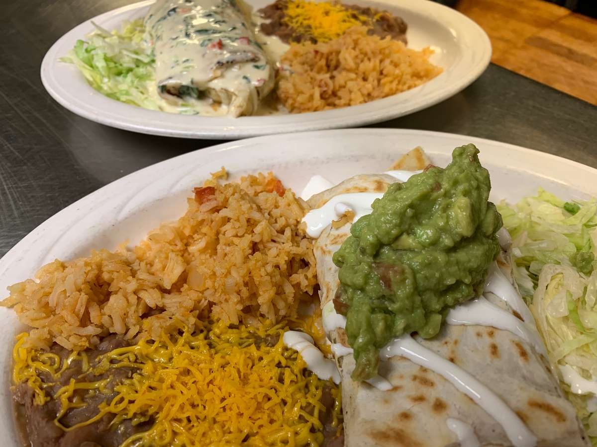sliced burrito on wooden board with tomatoes, guacamole, and sour cream