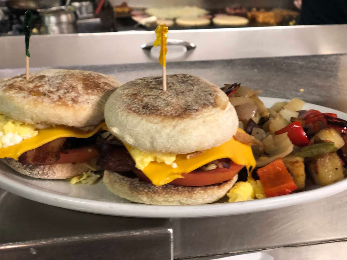 Toasted English muffin breakfast sandwich with American cheese, tomato, bacon & sausage