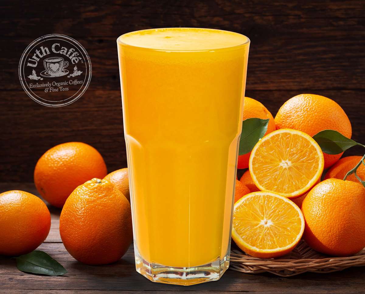 Glass of orange juice in front ot whole and cut oranges.