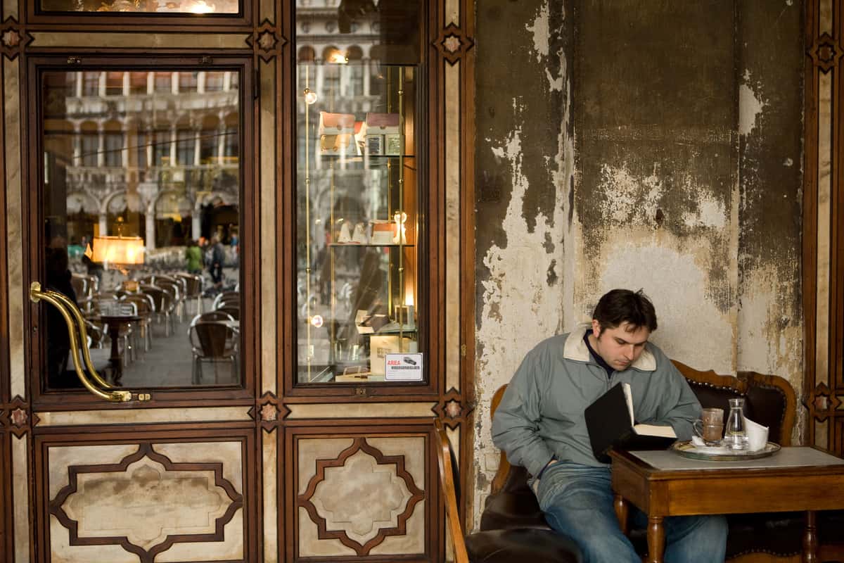 man reading a book at a table outside of an Italian cafe