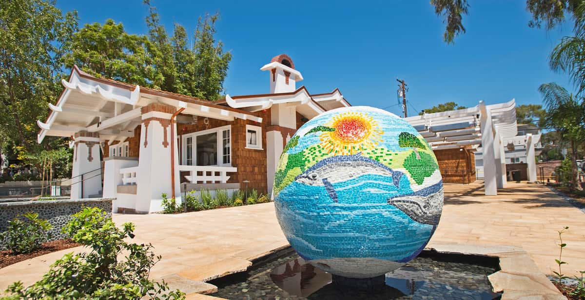 Shot of mosaic tile globe fountain with Urth Caffé and patio in background.