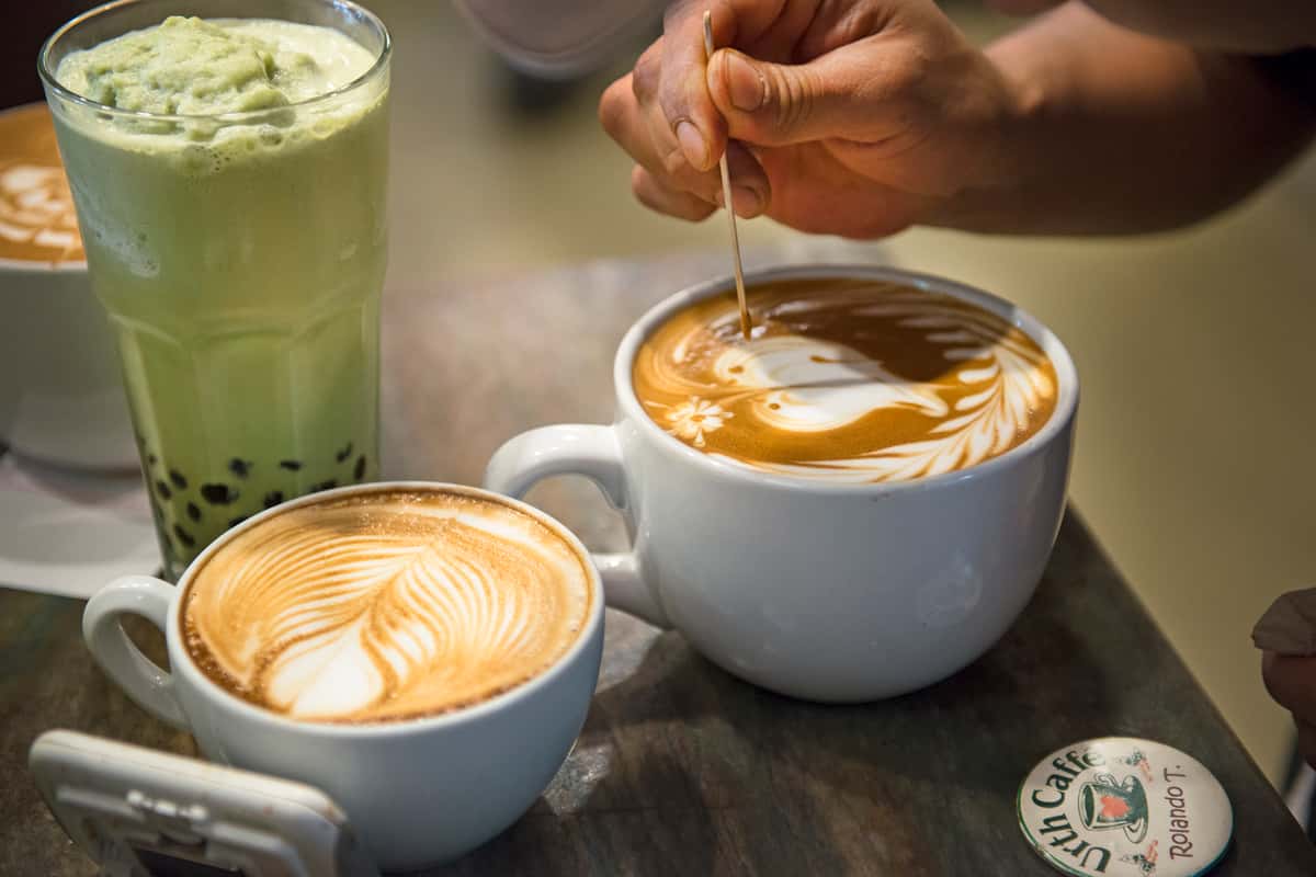 Three drinks, a blended ice matcha boba, a latte and another latte with barista etching a butterfly design into the foam