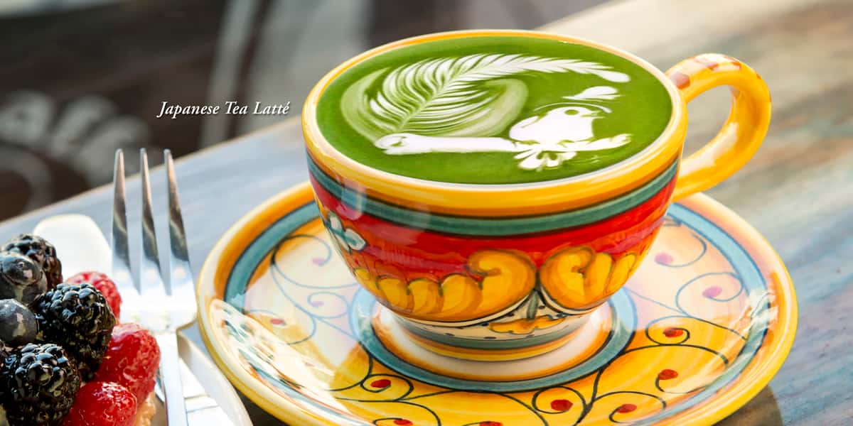 Decorative cup with Japanese Tea Latté with intricate green and white latté design is a perched songbird next to a fern.