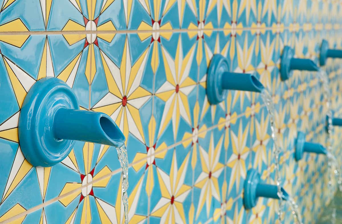 Closeup of tile fountain with star motifs in turquoise with water dripping from turquoise spouts