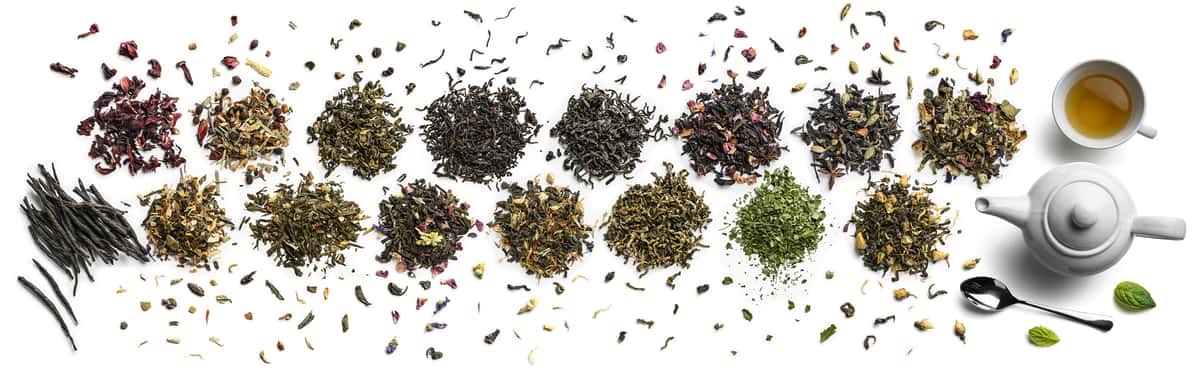 Looking down at two rows of little piles of loose tea of different colors with a white tea pot at the far right