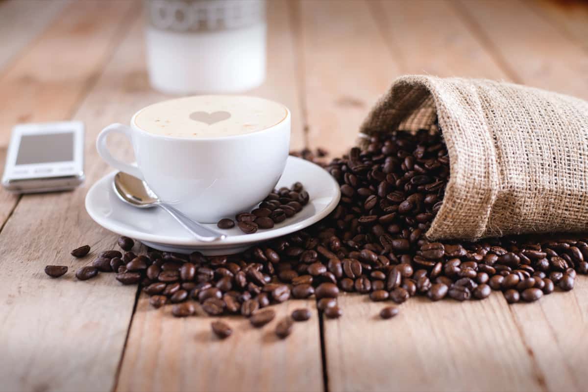 Spilled coffee beans surrounding a white coffee cup on a saucer