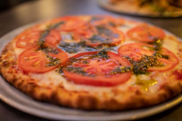 Pizza with sliced of tomato and pesto drizzled on top