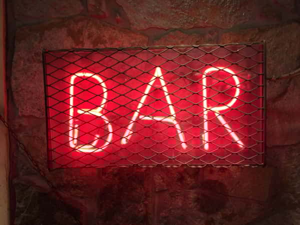Neon red bar sign covered by a grate