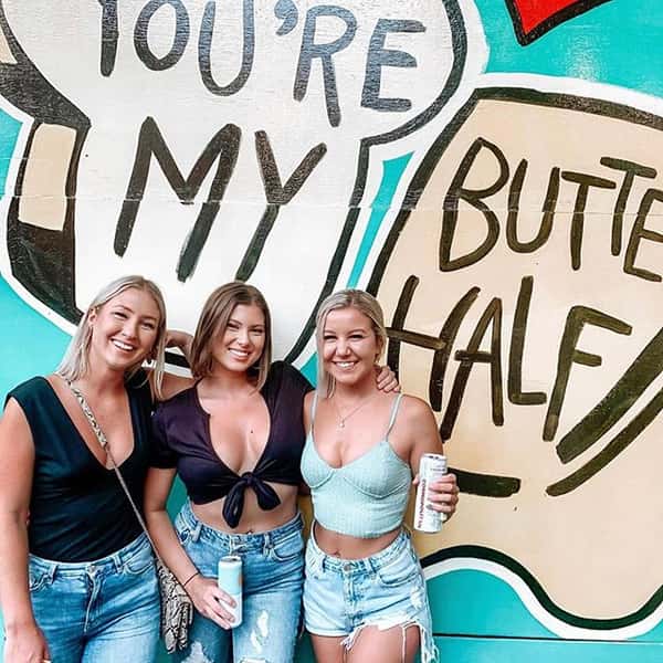 Three girls posing infront of a mural that says You're my buttered half!